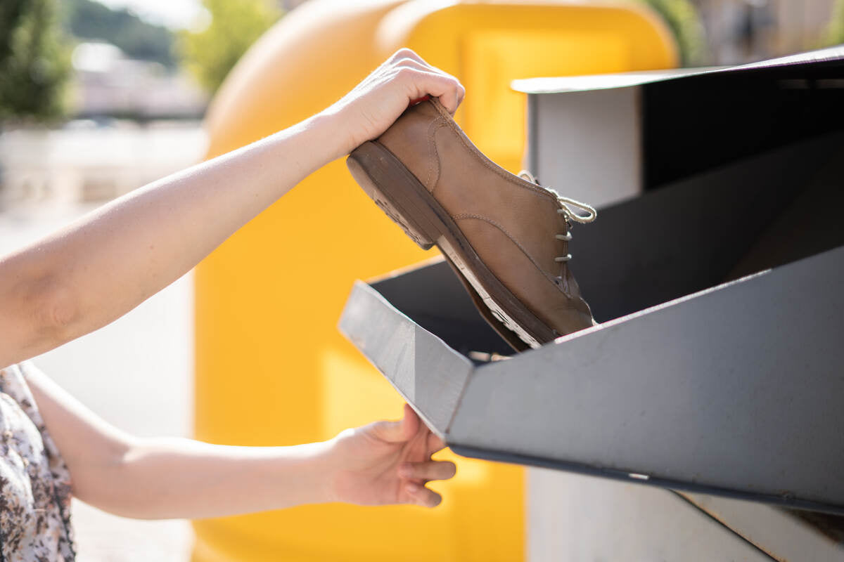 hands putting used shoes into clothing container for recycling